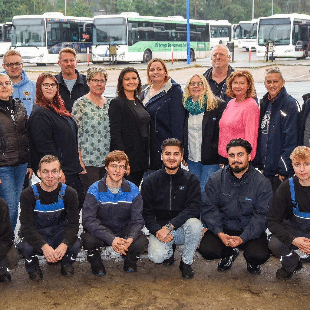 Group photo of some CeBus employees. Everyone is facing the camera and standing in 3 rows. The buses in the background.